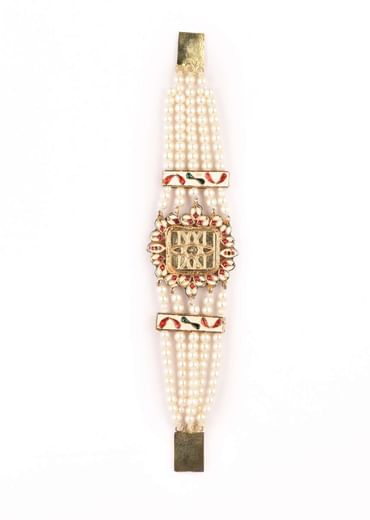 Gold Plated Bracelet With A Kundan Polki Centre Encrusted In A Red Stone And Multiple Moti Strings